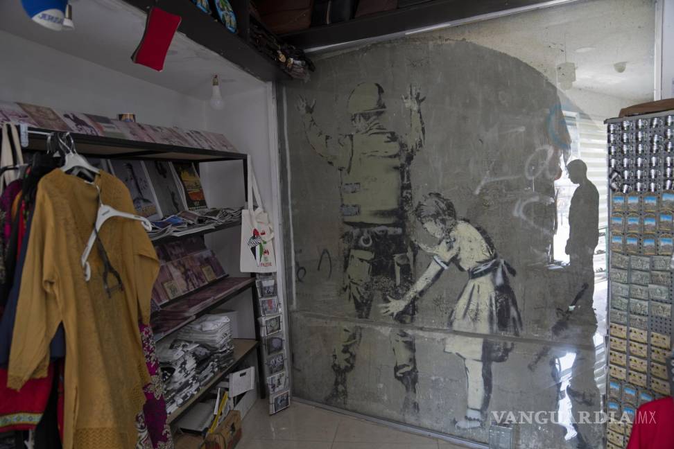 $!Un mural del reservado artista de grafiti británico Banksy está cubierto con vidrio protector dentro de una tienda de regalos, en la ciudad de Belén, Cisjordania.