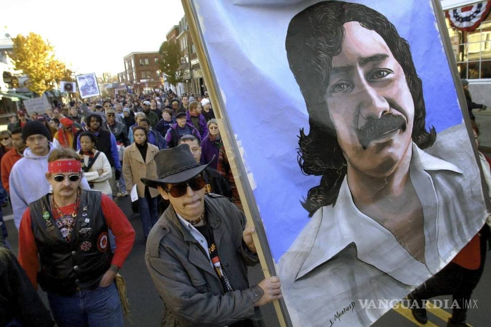 $!Manifestantes llevan una pintura del indio americano encarcelado Leonard Peltier durante una marcha por el Día Nacional del Luto en Plymouth, Massachusetts. AP/Steven Senne