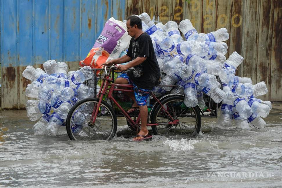 $!Un hombre utiliza su bicitaxi para transportar contenedores de plástico usados a lo largo de una calle inundada en la ciudad de Valenzuela, Filipinas.
