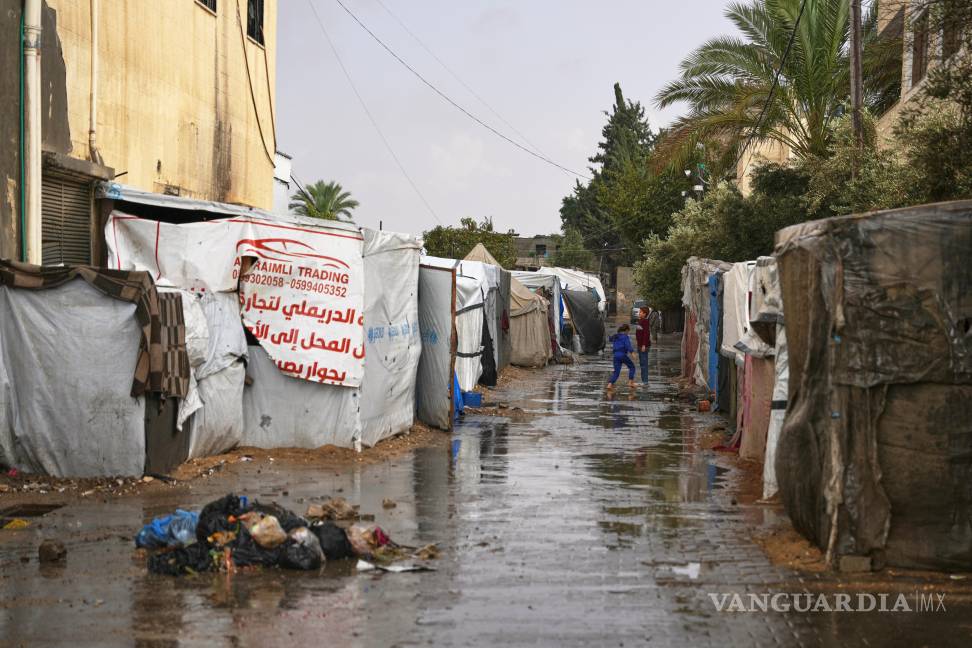 $!Niños palestinos caminan entre tiendas de campaña durante la lluvia en un campamento temporal en Deir al-Balah, en el centro de la Franja de Gaza.