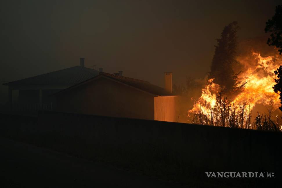 $!Un incendio forestal llega a una casa vacía mientras el humo oscurece el cielo en el pueblo de Bemposta, cerca de Ansiao, en el centro de Portugal.