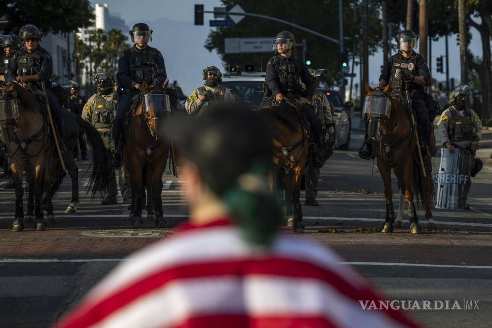 $!Agentes de policía, frente a manifestantes en el exterior del edificio del ayuntamiento durante protestas contra las redadas migratorias federales en Los Ángeles.