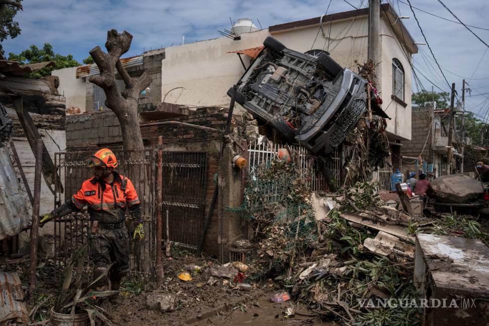 $!Un rescatista, miembro de la brigada de voluntarios Topos, trabaja junto a un automóvil colgado de una cerca junto a una casa dañada en Poza Rica.