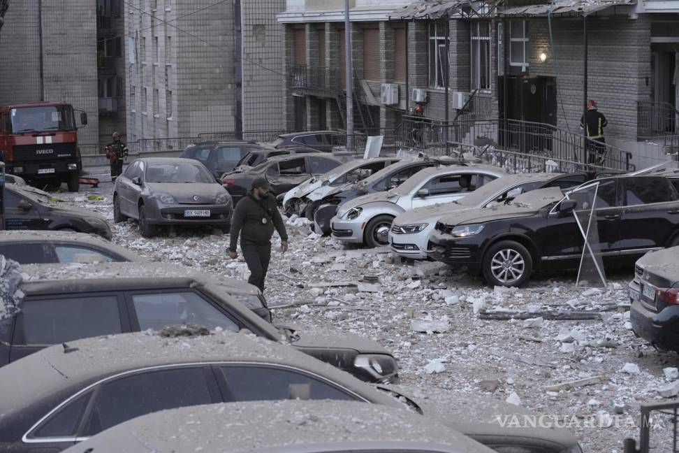 $!Un agente de policía camina por un estacionamiento con autos dañados, frente a un edificio de varias plantas, luego de un ataque ruso sobre Kiev.