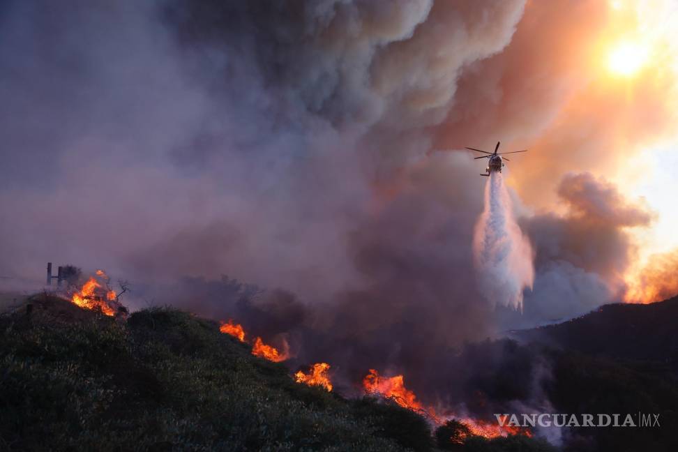 $!Un helicóptero arroja agua sobre el incendio Palisades que avanza en el vecindario Pacific Palisades de Los Ángeles, el martes 7 de enero de 2025.