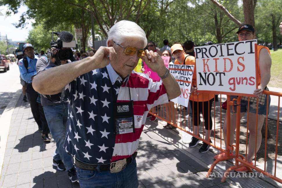 $!Un miembro de la Asociación Nacional del Rifle se tapa los oídos mientras camina junto a manifestantes durante la reunión anual de la NRA en Houston.