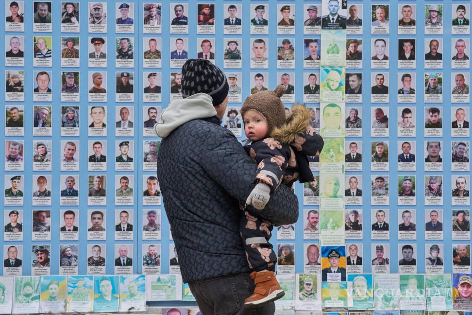 $!Un hombre sostiene a su hijo en el Muro Conmemorativo de los Defensores Caídos de Ucrania y muestra fotos de sus compañeros caídos en Kiev, Ucrania.