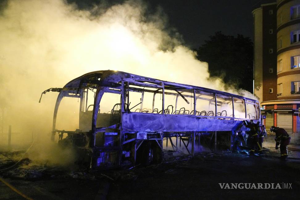 $!Bomberos arrojan agua a un autobús quemado, el sábado en un barrio en las afueras de París.