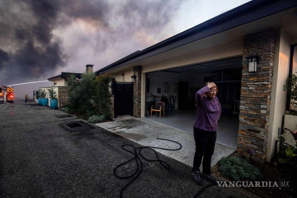 $!Una vecina se ve de pie delante de un garaje mientras los bomberos combaten el incendio de Palisades, en el vecindario de Pacific Palisades en Los Ángeles,.