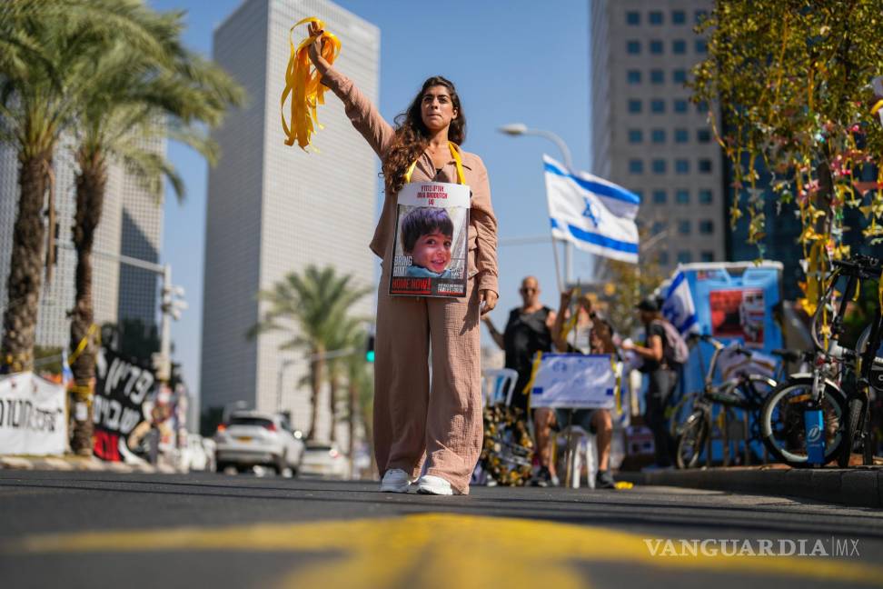 $!Una mujer, con la fotografía de un niño que es rehén de Hamás en Israel, entrega listones amarillos a los automovilistas en el centro de Tel Aviv, Israel.