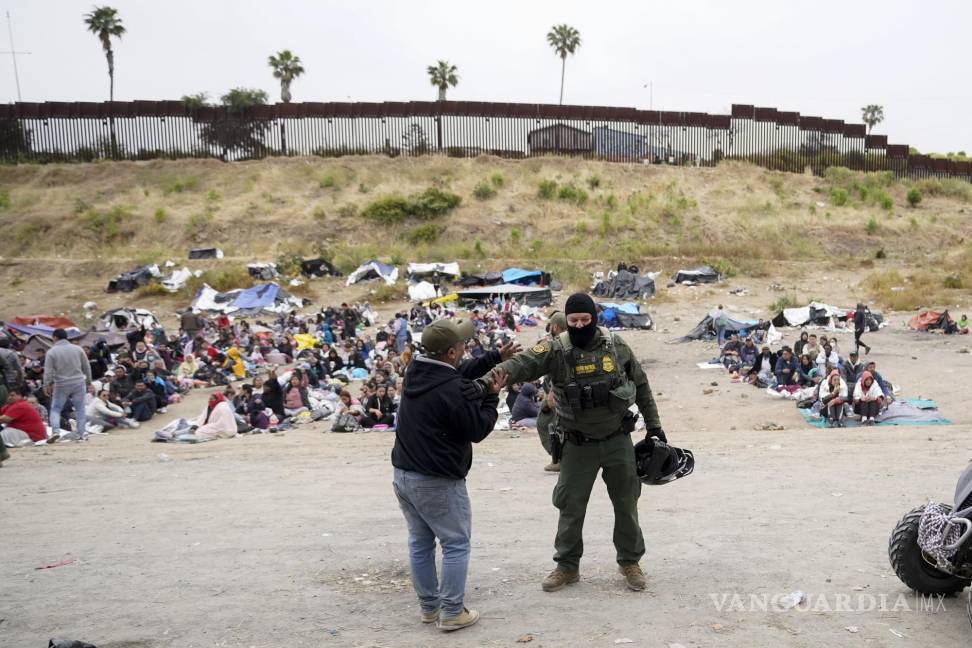 $!Un hombre bromea con un agente de la Patrulla Fronteriza mientras él y otros migrantes aguardan para solicitar asilo en San Diego.