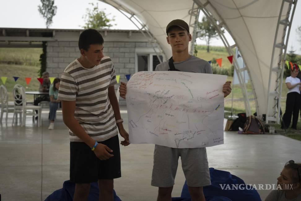 $!Oleksandr Hryshchenko (I) observa a Valerii Soldatenko, de 16 años, mostrar una pancarta que dice “recursos de vida” en el campamento de rehabilitación