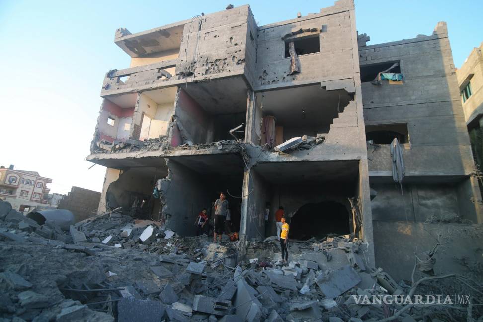 $!Palestinos de pie junto a un edificio destruido en un ataque aéreo israelí en la frontera de Rafah, en la Franja de Gaza, el lunes 16 de octubre de 2023.
