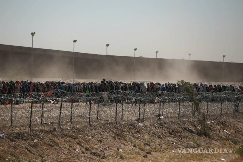 $!Migrantes alineados entre una valla con alambre de púas y el muro fronterizo entre Estados Unidos y México, visto desde Ciudad Juárez, México.