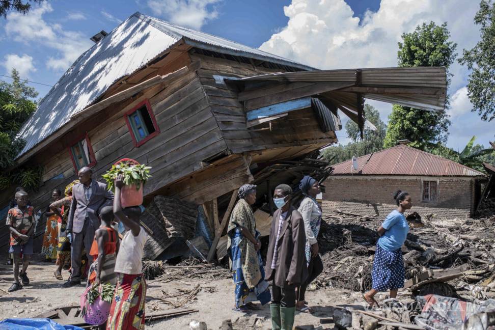 $!La gente camina junto a una casa destruida por las inundaciones en la aldea de Nyamukubi.