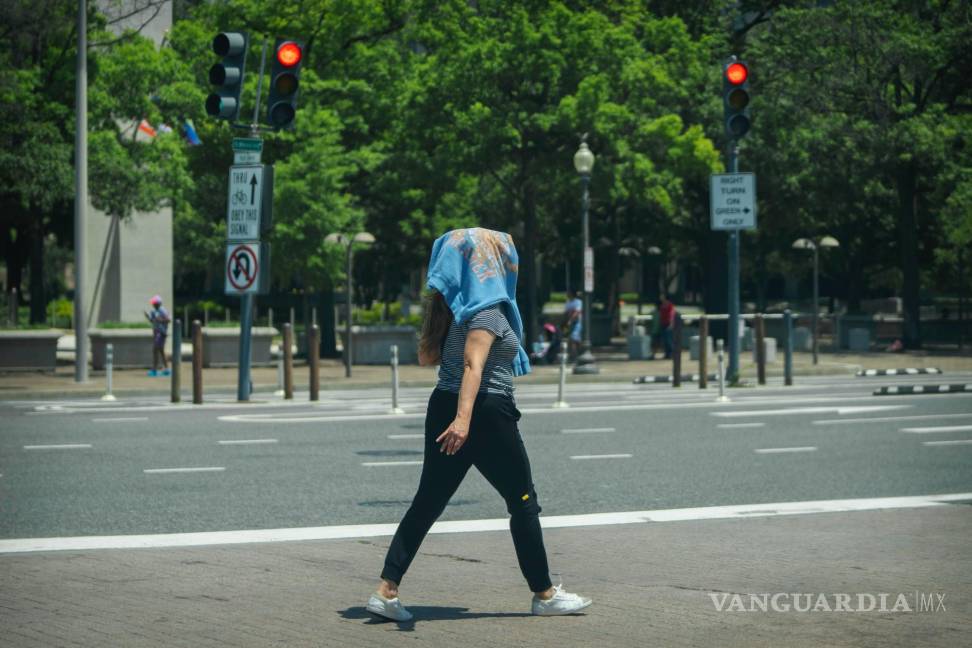 $!Una mujer camina con una sudadera en la cabeza para protegerse del sol en el centro de Washington, el miércoles 19 de junio de 2024.
