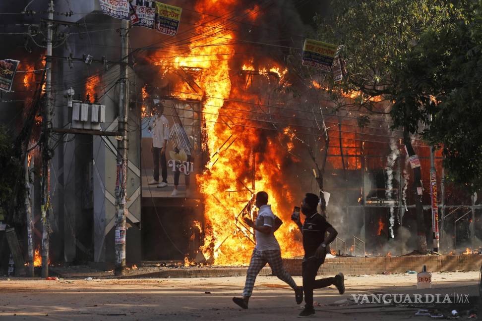 $!Los hombres corren frente a un centro comercial que fue incendiado durante una manifestación contra la Primera Ministra Sheikh Hasina.