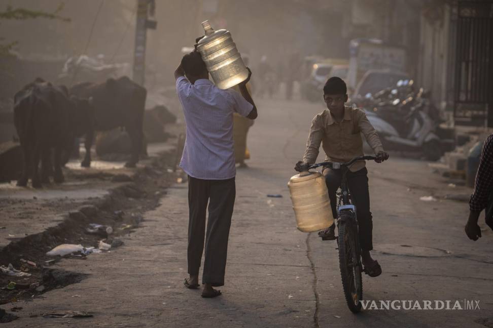 $!Un hombre lleva un recipiente para el agua mientras un niño anda en bicicleta para recoger agua de un camión cisterna móvil en Nueva Delhi, India.
