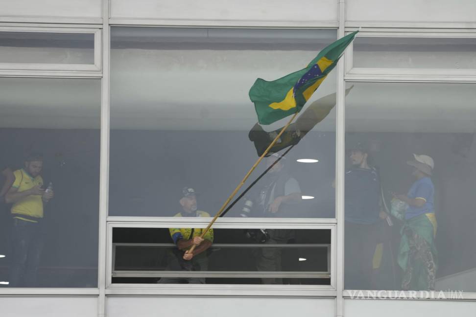 $!Un manifestante, partidario del expresidente brasileño Jair Bolsonaro, ondea una bandera brasileña desde una ventana tras asaltar el Palacio Planalto en Brasilia.