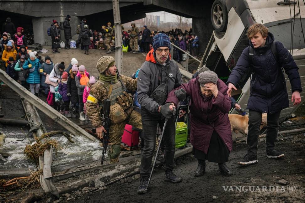 $!Una anciana es ayudada a cruzar el río Irpin por un camino debajo de un puente que fue destruido por las tropas ucranianas para frenar el avance del ejército ruso.