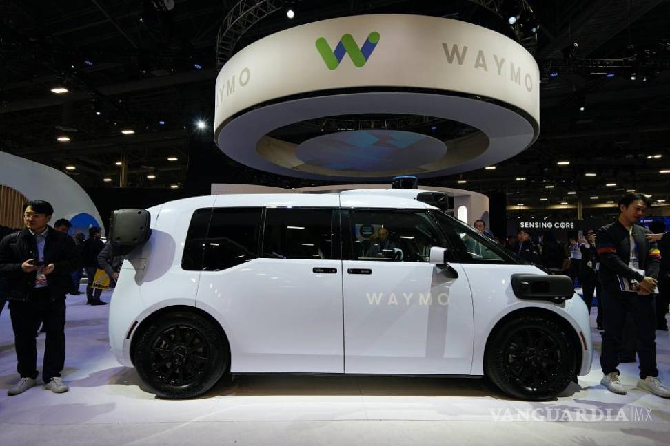 $!Varias personas observan un vehículo Zeekr RT con el controlador Waymo de sexta generación en exhibición en el stand de Waymo en la CES 2025.