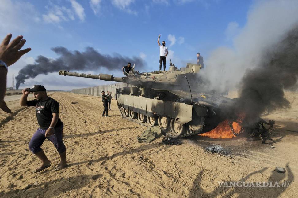 $!Palestinos celebran junto a un tanque israelí destruido en la cerca fronteriza de la Franja de Gaza, al este de Jan Yunis, en el sur del enclave, el 7 de octubre de 2023.