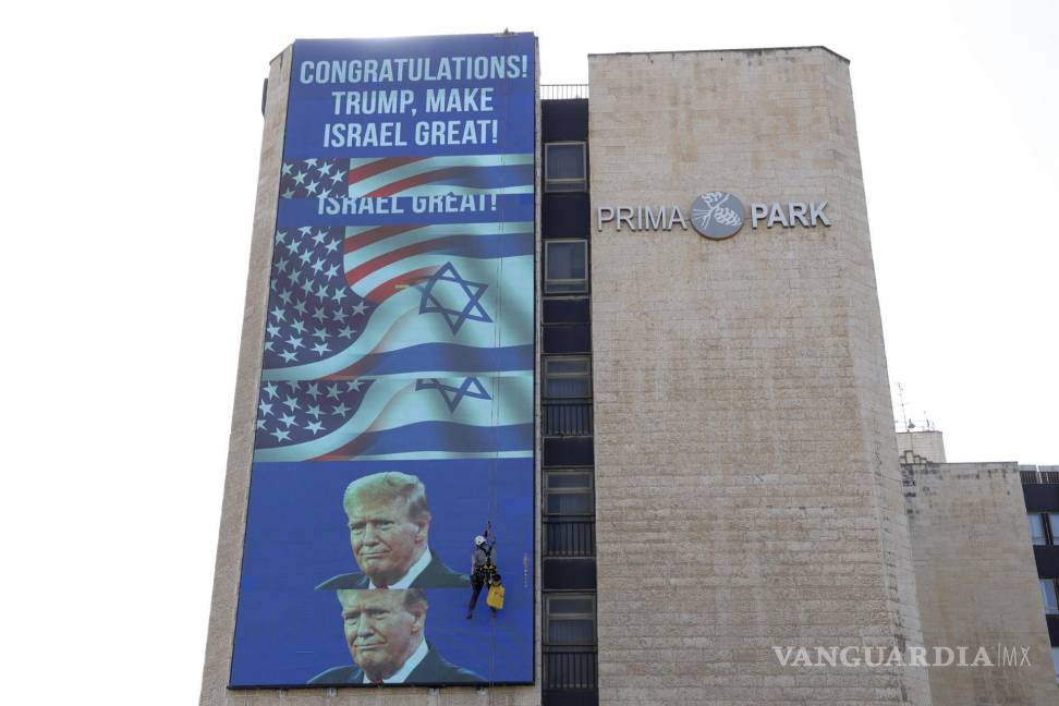 $!Un trabajador colgado en un edificio en el que se exhibe un gran cartel de felicitación a Donald Trump, a la entrada de Jerusalén.