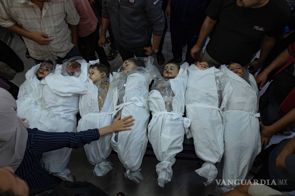 $!Gente de pie en torno a cuerpos de niños muertos en un bombardeo israelí en la Franja de Gaza, en una morgue en Jan Yunis, el jueves 19 de octubre de 2023.
