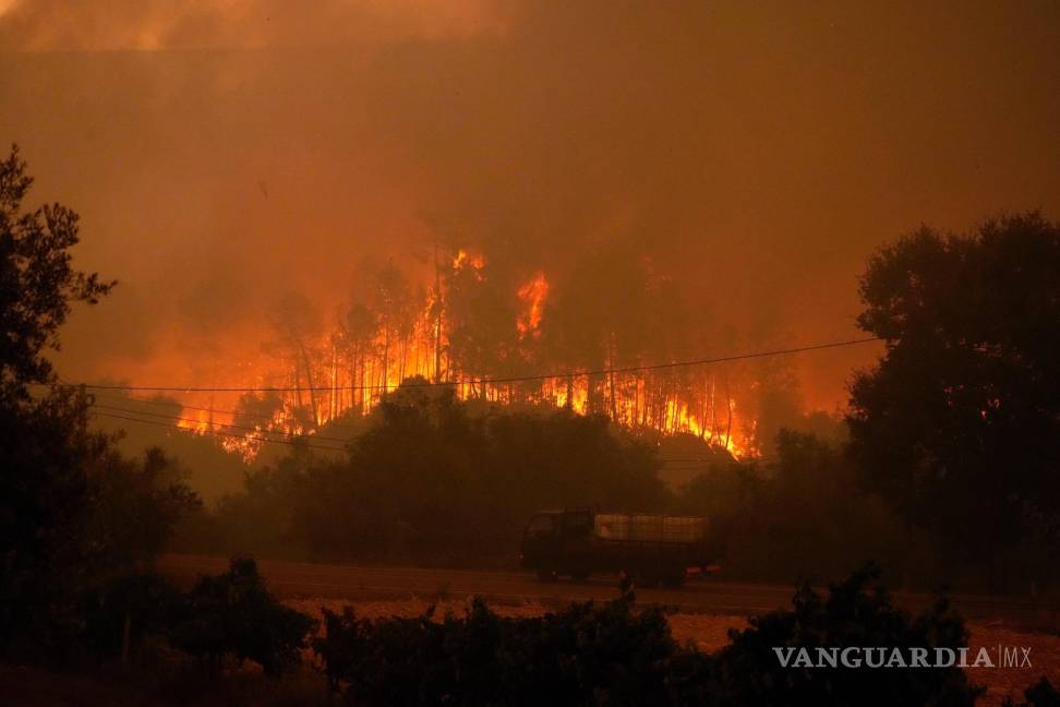 $!Un camión que transportaba tanques con agua pasa junto a un incendio forestal en el pueblo de Bemposta, cerca de Ansiao, en el centro de Portugal.