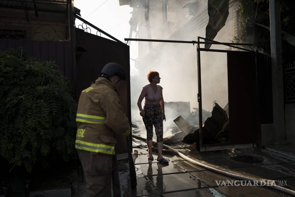 $!Una mujer sale de su casa en llamas mientras los bomberos trabajan para extinguir el fuego después de un ataque ruso en Kherson, Ucrania.