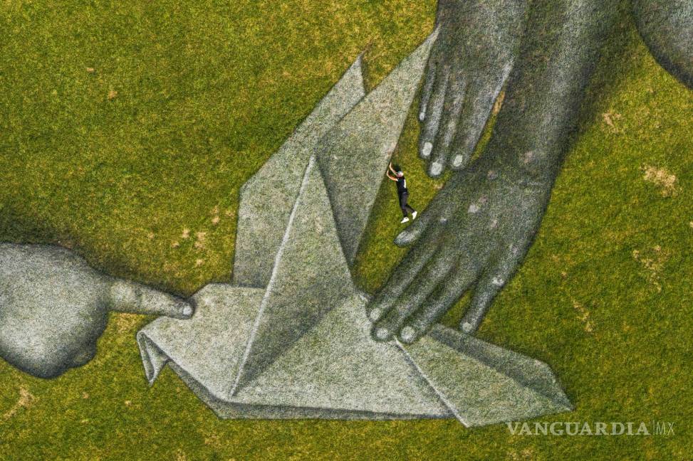 $!El artista suizo-francés Saype (Guillaume Legros) posa en su gigantesco cuadro efímero de arte terrestre titulado “Mundo en progreso II” que representa a dos niños dibujando y construyendo con origami su mundo ideal, en la Sede de las Naciones Unidas (ONU) en Nueva York. AP/Valentin Flauraud/Keystone