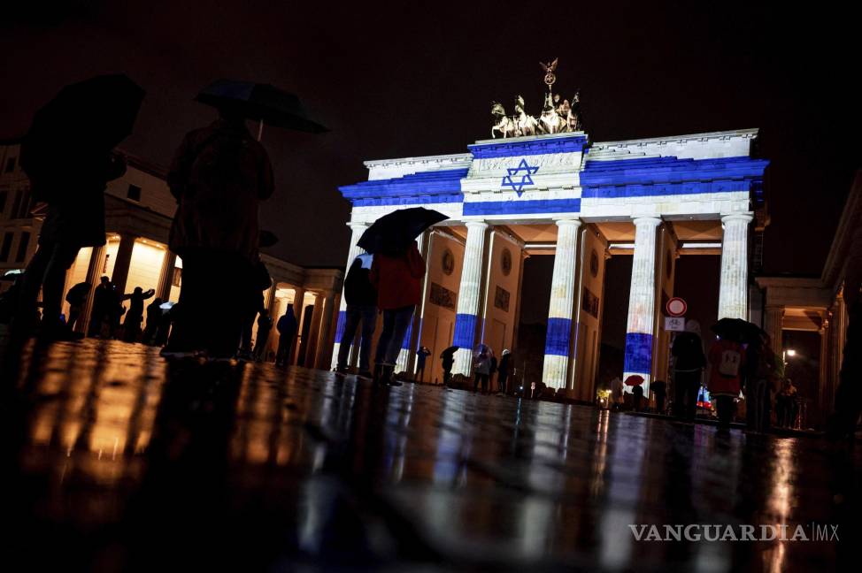 $!Personas observan la Puerta de Brandenburgo se ilumina con los colores de la bandera israelí como muestra de solidaridad, en Berlín, Alemania.