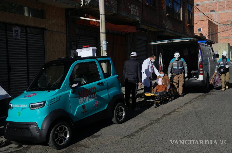 $!El Dr. Carlos Ortuno atiende a Juana Velasco flanqueado por un auto eléctrico Quantum de fabricación boliviana y una ambulancia, en La Paz, Bolivia.