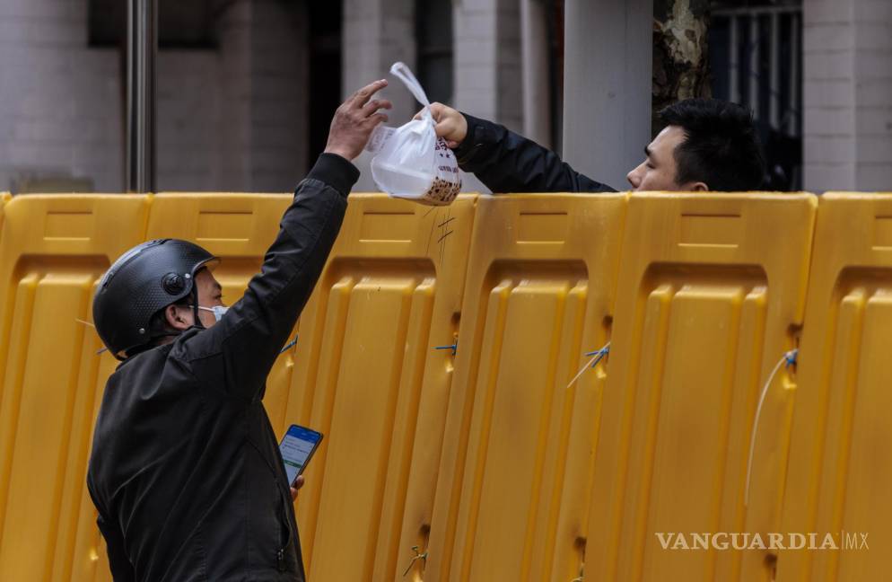 $!Un hombre entrega comida a un hombre en el complejo en cuarentena en medio del cierre, en el lado de Puxi de la ciudad, en Shanghái, China.