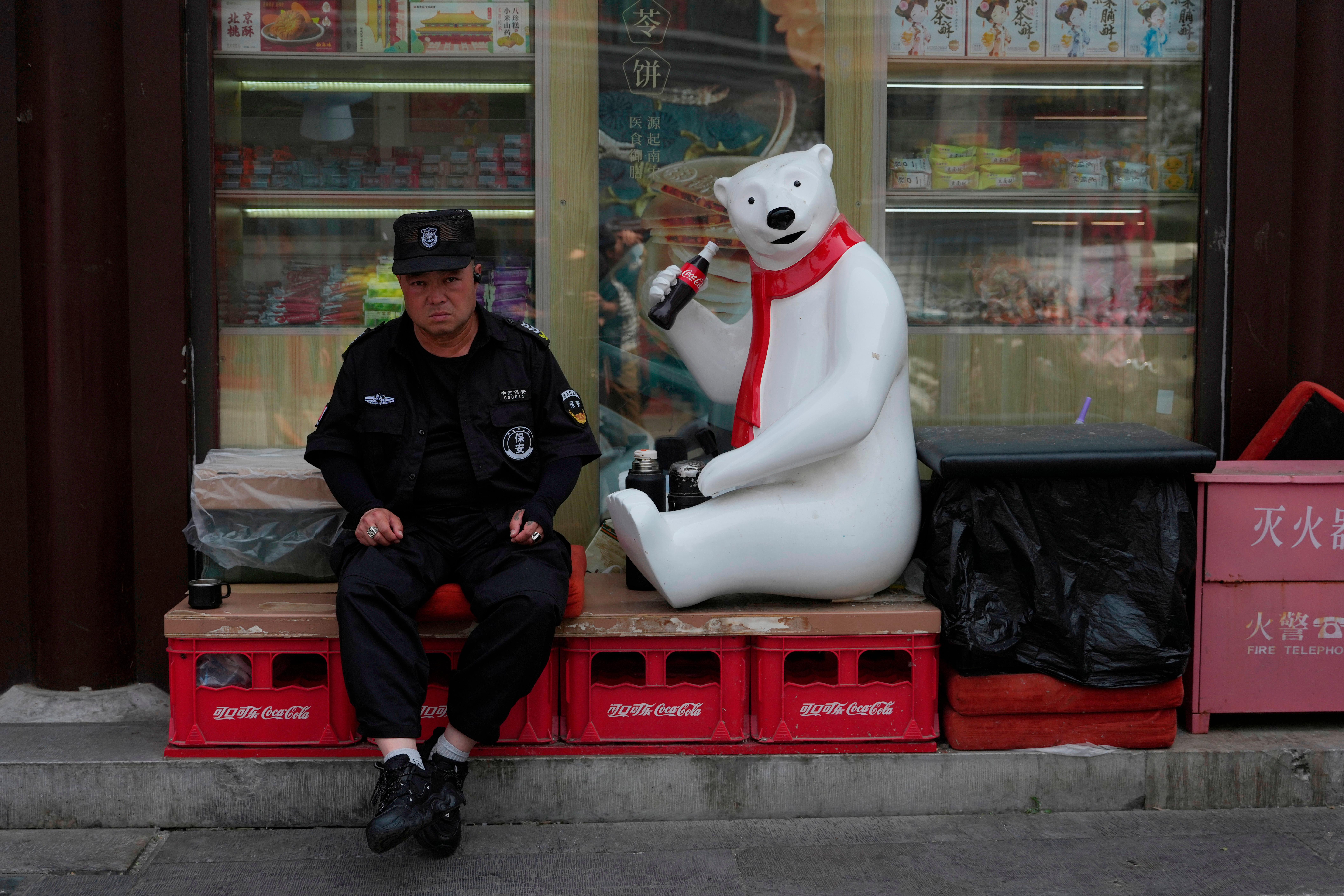 n guardia de seguridad descansa cerca de la mascota de Coca-Cola frente a una tienda a la llegada del presidente estadounidense Donald Trump a Pekín.