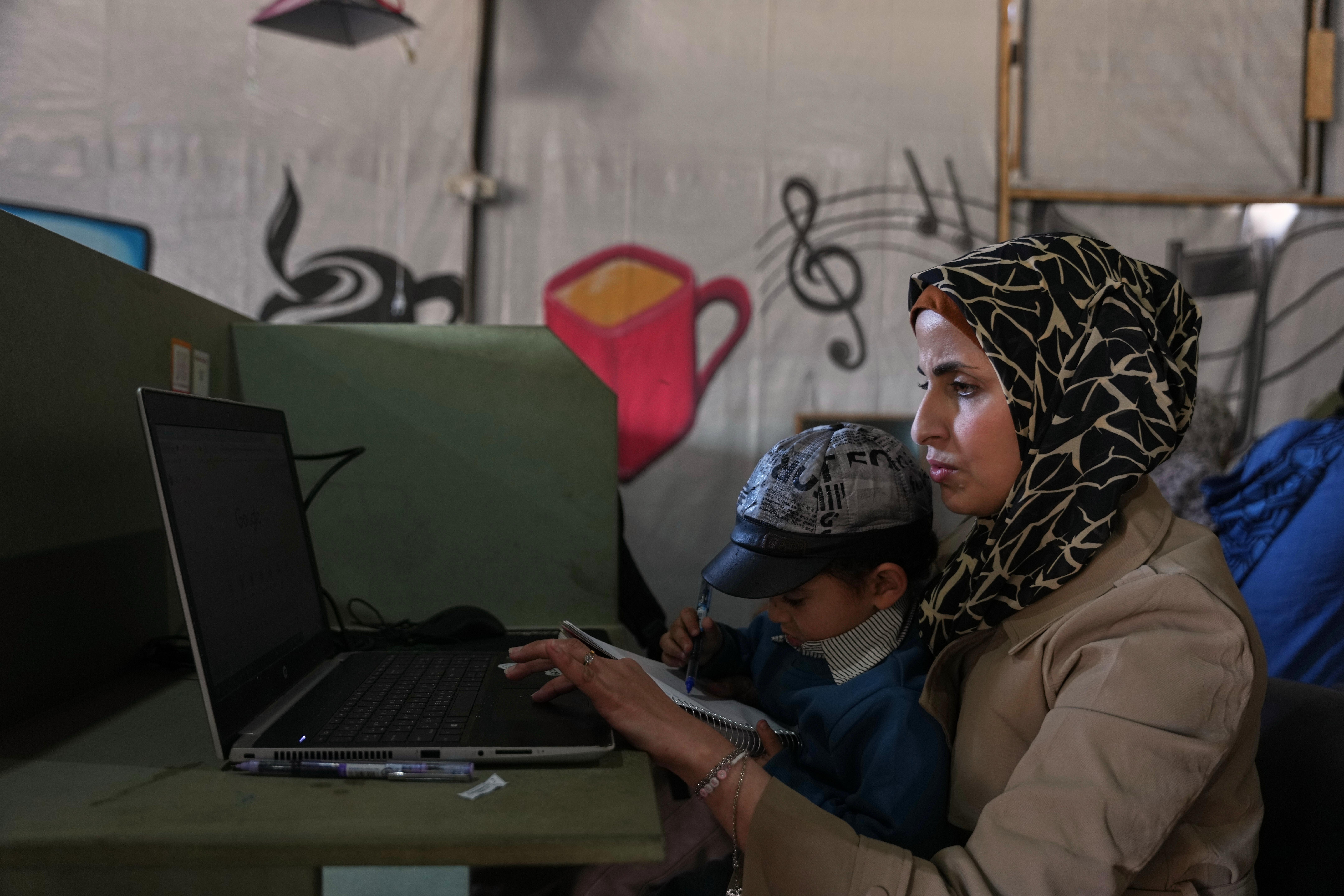 La diseñadora gráfica palestina Reem Alkhateebtrabaja en su computadora junto a su hijo en un espacio de coworking en Jan Yunis, sur de la Franja de Gaza.