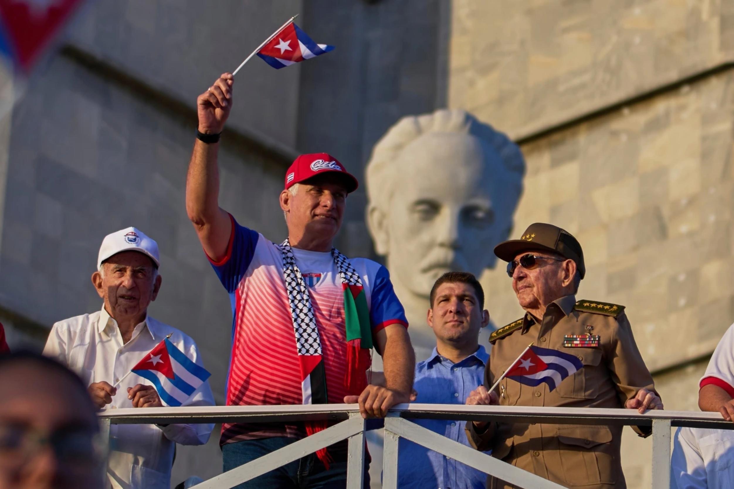 El presidente de Cuba, Miguel Díaz-Canel, levanta una bandera cubana Een el desfile del Primero de Mayo junto a Raúl Castro, el 1 de mayo de 2025.